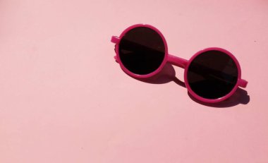 Pembe yuvarlak, güzel güneş gözlüklü kız. Pembe çerçeveli siyah mercekli glesler. Pembe pastel arka planda izole edilmiş.
