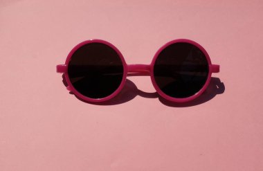 Pembe yuvarlak, güzel güneş gözlüklü kız. Pembe çerçeveli siyah mercekli glesler. Pembe pastel arka planda izole edilmiş.