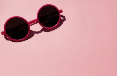 Pembe yuvarlak, güzel güneş gözlüklü kız. Pembe çerçeveli siyah mercekli glesler. Pembe pastel arka planda izole edilmiş.