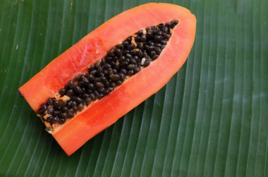 Üst ve düz bir zemin üzerinde yeşil muz yapraklarına izole edilmiş dilimlenmiş yeşil yapraklı olgun papaya meyveli papaya uzanır. Sağlıklı beslenme için sebze ve meyve.