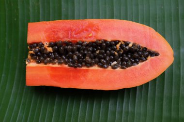Üst ve düz bir zemin üzerinde yeşil muz yapraklarına izole edilmiş dilimlenmiş yeşil yapraklı olgun papaya meyveli papaya uzanır. Sağlıklı beslenme için sebze ve meyve.