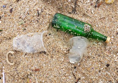Çöp kutusunu kapatın. Kumlu sahilde kıyıya vuran kullanılmış bir cam şişe. Çevre kirliliği, Dünya günü, ekolojik sorunlar, gezegeni korumak, doğa koruma, deniz kirliliği.