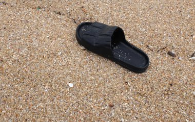 Kumlu sahilde tek bir siyah parmak arası terlik ve kıyıya vuran dalgalar. Yaz tatili ve tropikal tatil konsepti.