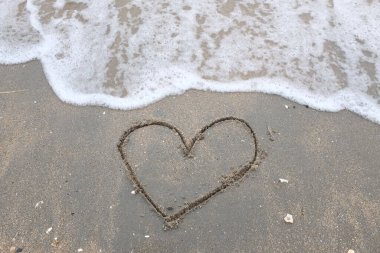 Gün batımında kumsala çizilen kalp. Güzel bir deniz manzarası. Kum sanatı şeklinde desenli deniz dalgaları. Kalp sembolü. Sevgi. Deniz köpüğü. Sevgililer Günü konsepti.