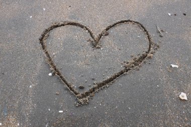 Günbatımında ıslak kumsalda kahverengi bir kalp çizildi. Çok güzel bir deniz manzarası. Kum sanatı şeklinde desen deniz dalgaları. Kalp sembolü. Sevgi. Deniz köpüğü. Sevgililer Günü konsepti.