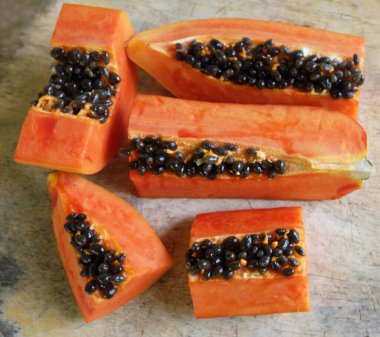 Üst ve düz taze, olgun bir papaya meyvesi uzanıyor tohumlarla, yemek dokusuyla, kesilmiş, dilimlenmiş meyvelerle ahşap kesim tahtasına. Sağlıklı beslenme için sebze ve meyve