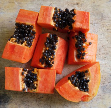 Üst ve düz taze, olgun bir papaya meyvesi uzanıyor tohumlarla, yemek dokusuyla, kesilmiş, dilimlenmiş meyvelerle ahşap kesim tahtasına. Sağlıklı beslenme için sebze ve meyve