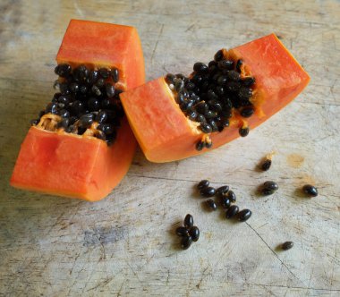 Üst ve düz taze, olgun bir papaya meyvesi uzanıyor tohumlarla, yemek dokusuyla, kesilmiş, dilimlenmiş meyvelerle ahşap kesim tahtasına. Sağlıklı beslenme için sebze ve meyve