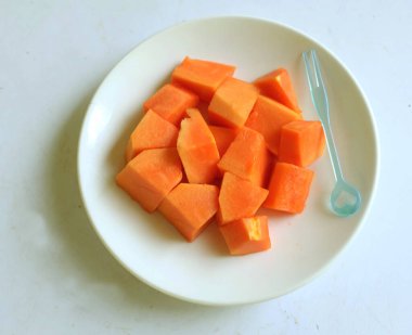 Üst ve düz taze, olgun bir papaya meyvesi uzanıyor. Tohumları, yemek dokusunu, dilimlenmiş meyveleri beyaz seramik bir tabakta izole edilmiş. Sağlıklı beslenme için sebze ve meyve