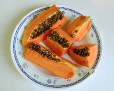 Üst ve düz taze, olgun bir papaya meyvesi uzanıyor. Tohumları, yemek dokusunu, dilimlenmiş meyveleri beyaz seramik bir tabakta izole edilmiş. Sağlıklı beslenme için sebze ve meyve