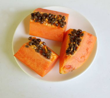 Üst ve düz taze, olgun bir papaya meyvesi uzanıyor. Tohumları, yemek dokusunu, dilimlenmiş meyveleri beyaz seramik bir tabakta izole edilmiş. Sağlıklı beslenme için sebze ve meyve