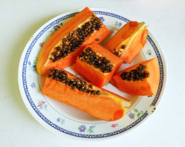 Üst ve düz taze, olgun bir papaya meyvesi uzanıyor. Tohumları, yemek dokusunu, dilimlenmiş meyveleri beyaz seramik bir tabakta izole edilmiş. Sağlıklı beslenme için sebze ve meyve