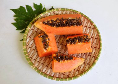 Üst ve düz taze, olgun bir papaya meyvesi uzanıyor tohumlarla, yemek dokusuyla, kesilmiş, dilimlenmiş meyveler ahşap tepside izole edilmiş. Sağlıklı beslenme için sebze ve meyve