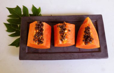 Üst ve düz taze, olgun bir papaya meyvesi uzanıyor tohumlarla, yemek dokusuyla, dilimlenmiş, siyah dikdörtgen bir tabakta izole edilmiş meyvelerle. Sağlıklı beslenme için sebze ve meyve