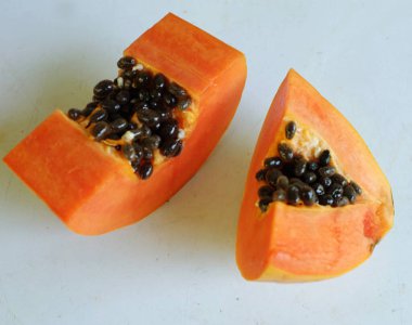 Üst ve düz taze, olgun bir papaya meyvesi uzanıyor. Tohumları, yemek dokusunu, kesimini, kesilmiş meyveleri beyaz bir zeminde izole edilmiş. Sağlıklı beslenme için sebze ve meyve.