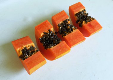 Üst ve düz taze, olgun bir papaya meyvesi uzanıyor. Tohumları, yemek dokusunu, kesimini, kesilmiş meyveleri beyaz bir zeminde izole edilmiş. Sağlıklı beslenme için sebze ve meyve.