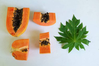 Üst ve düz taze, olgun bir papaya meyvesi uzanıyor. Tohumları, yemek dokusunu, kesimini, kesilmiş meyveleri beyaz bir zeminde izole edilmiş. Sağlıklı beslenme için sebze ve meyve.