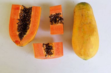 Üst ve düz taze, olgun bir papaya meyvesi uzanıyor. Tohumları, yemek dokusunu, kesimini, kesilmiş meyveleri beyaz bir zeminde izole edilmiş. Sağlıklı beslenme için sebze ve meyve.