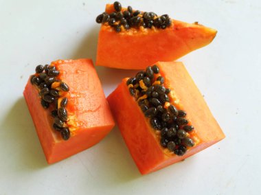 Üst ve düz taze, olgun bir papaya meyvesi uzanıyor. Tohumları, yemek dokusunu, kesimini, kesilmiş meyveleri beyaz bir zeminde izole edilmiş. Sağlıklı beslenme için sebze ve meyve.