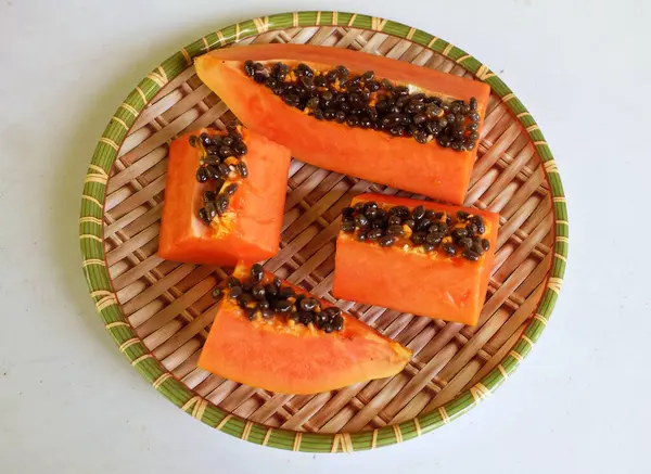 Üst ve düz taze, olgun bir papaya meyvesi uzanıyor tohumlarla, yemek dokusuyla, kesilmiş, dilimlenmiş meyveler ahşap tepside izole edilmiş. Sağlıklı beslenme için sebze ve meyve