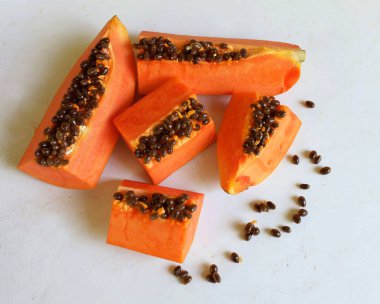 Üst ve düz taze, olgun bir papaya meyvesi uzanıyor. Tohumları, yemek dokusunu, kesimini, kesilmiş meyveleri beyaz bir zeminde izole edilmiş. Sağlıklı beslenme için sebze ve meyve