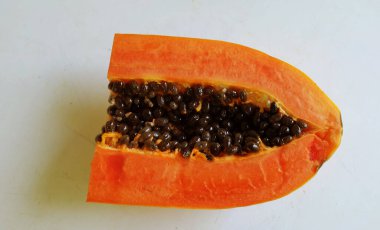 Üst ve düz taze, olgun bir papaya meyvesi uzanıyor. Tohumları, yemek dokusunu, kesimini, kesilmiş meyveleri beyaz bir zeminde izole edilmiş. Sağlıklı beslenme için sebze ve meyve
