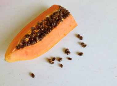 Üst ve düz taze, olgun bir papaya meyvesi uzanıyor. Tohumları, yemek dokusunu, kesimini, kesilmiş meyveleri beyaz bir zeminde izole edilmiş. Sağlıklı beslenme için sebze ve meyve