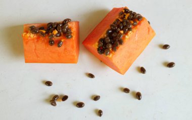 Üst ve düz taze, olgun bir papaya meyvesi uzanıyor. Tohumları, yemek dokusunu, kesimini, kesilmiş meyveleri beyaz bir zeminde izole edilmiş. Sağlıklı beslenme için sebze ve meyve