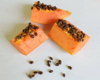 Üst ve düz taze, olgun bir papaya meyvesi uzanıyor. Tohumları, yemek dokusunu, kesimini, kesilmiş meyveleri beyaz bir zeminde izole edilmiş. Sağlıklı beslenme için sebze ve meyve