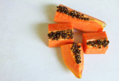 Üst ve düz taze, olgun bir papaya meyvesi uzanıyor. Tohumları, yemek dokusunu, kesimini, kesilmiş meyveleri beyaz bir zeminde izole edilmiş. Sağlıklı beslenme için sebze ve meyve
