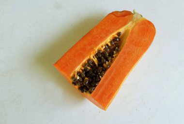 Üst ve düz taze, olgun bir papaya meyvesi uzanıyor. Tohumları, yemek dokusunu, kesimini, kesilmiş meyveleri beyaz bir zeminde izole edilmiş. Sağlıklı beslenme için sebze ve meyve