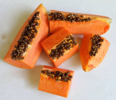 Üst ve düz taze, olgun bir papaya meyvesi uzanıyor. Tohumları, yemek dokusunu, kesimini, kesilmiş meyveleri beyaz bir zeminde izole edilmiş. Sağlıklı beslenme için sebze ve meyve