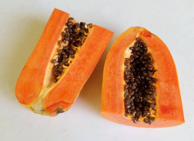 Üst ve düz taze, olgun bir papaya meyvesi uzanıyor. Tohumları, yemek dokusunu, kesimini, kesilmiş meyveleri beyaz bir zeminde izole edilmiş. Sağlıklı beslenme için sebze ve meyve