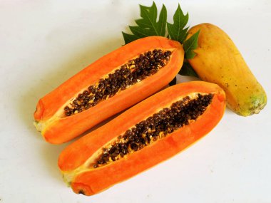 Üst ve düz taze, olgun bir papaya meyvesi uzanıyor. Tohumları, yemek dokusunu, kesimini, kesilmiş meyveleri beyaz bir zeminde izole edilmiş. Sağlıklı beslenme için sebze ve meyve