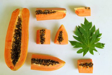 Üst ve düz taze, olgun bir papaya meyvesi uzanıyor. Tohumları, yemek dokusunu, kesimini, kesilmiş meyveleri beyaz bir zeminde izole edilmiş. Sağlıklı beslenme için sebze ve meyve