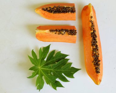 Üst ve düz taze, olgun bir papaya meyvesi uzanıyor. Tohumları, yemek dokusunu, kesimini, kesilmiş meyveleri beyaz bir zeminde izole edilmiş. Sağlıklı beslenme için sebze ve meyve