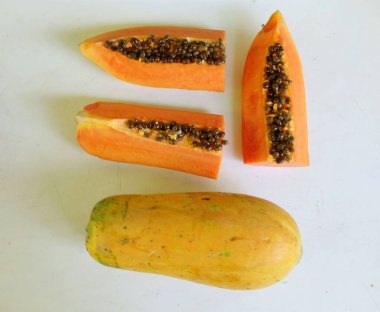 Üst ve düz taze, olgun bir papaya meyvesi uzanıyor. Tohumları, yemek dokusunu, kesimini, kesilmiş meyveleri beyaz bir zeminde izole edilmiş. Sağlıklı beslenme için sebze ve meyve