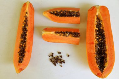 Üst ve düz taze, olgun bir papaya meyvesi uzanıyor. Tohumları, yemek dokusunu, kesimini, kesilmiş meyveleri beyaz bir zeminde izole edilmiş. Sağlıklı beslenme için sebze ve meyve