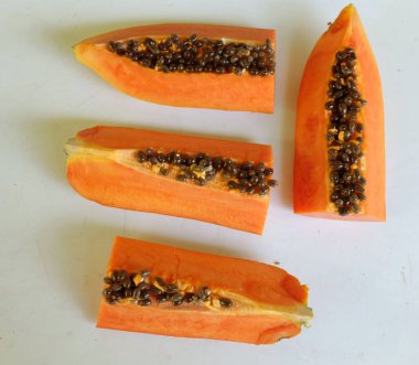 Üst ve düz taze, olgun bir papaya meyvesi uzanıyor. Tohumları, yemek dokusunu, kesimini, kesilmiş meyveleri beyaz bir zeminde izole edilmiş. Sağlıklı beslenme için sebze ve meyve