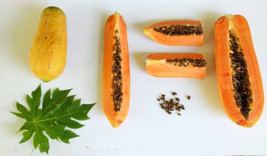 Üst ve düz taze, olgun bir papaya meyvesi uzanıyor. Tohumları, yemek dokusunu, kesimini, kesilmiş meyveleri beyaz bir zeminde izole edilmiş. Sağlıklı beslenme için sebze ve meyve