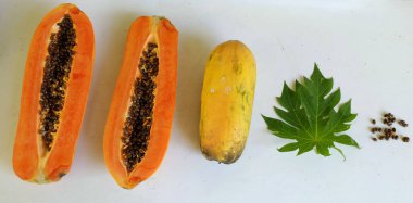 Üst ve düz taze, olgun bir papaya meyvesi uzanıyor. Tohumları, yemek dokusunu, kesimini, kesilmiş meyveleri beyaz bir zeminde izole edilmiş. Sağlıklı beslenme için sebze ve meyve