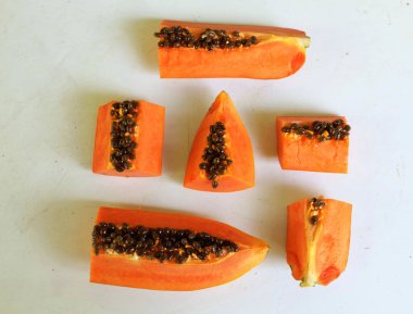 Üst ve düz taze, olgun bir papaya meyvesi uzanıyor. Tohumları, yemek dokusunu, kesimini, kesilmiş meyveleri beyaz bir zeminde izole edilmiş. Sağlıklı beslenme için sebze ve meyve
