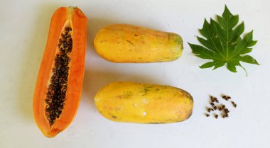Üst ve düz taze, olgun bir papaya meyvesi uzanıyor. Tohumları, yemek dokusunu, kesimini, kesilmiş meyveleri beyaz bir zeminde izole edilmiş. Sağlıklı beslenme için sebze ve meyve