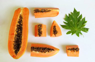 Üst ve düz taze, olgun bir papaya meyvesi uzanıyor. Tohumları, yemek dokusunu, kesimini, kesilmiş meyveleri beyaz bir zeminde izole edilmiş. Sağlıklı beslenme için sebze ve meyve