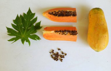Üst ve düz taze, olgun bir papaya meyvesi uzanıyor. Tohumları, yemek dokusunu, kesimini, kesilmiş meyveleri beyaz bir zeminde izole edilmiş. Sağlıklı beslenme için sebze ve meyve
