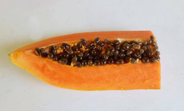 Üst ve düz taze, olgun bir papaya meyvesi uzanıyor. Tohumları, yemek dokusunu, kesimini, kesilmiş meyveleri beyaz bir zeminde izole edilmiş. Sağlıklı beslenme için sebze ve meyve