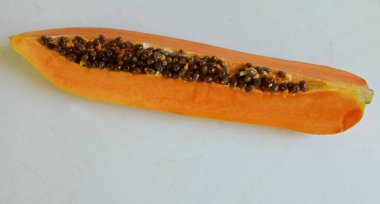 Üst ve düz taze, olgun bir papaya meyvesi uzanıyor. Tohumları, yemek dokusunu, kesimini, kesilmiş meyveleri beyaz bir zeminde izole edilmiş. Sağlıklı beslenme için sebze ve meyve