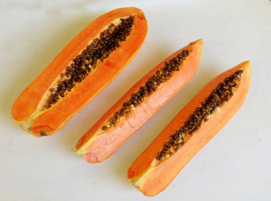 Üst ve düz taze, olgun bir papaya meyvesi uzanıyor. Tohumları, yemek dokusunu, kesimini, kesilmiş meyveleri beyaz bir zeminde izole edilmiş. Sağlıklı beslenme için sebze ve meyve