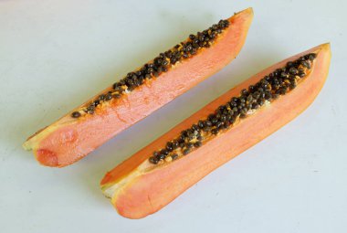 Üst ve düz taze, olgun bir papaya meyvesi uzanıyor. Tohumları, yemek dokusunu, kesimini, kesilmiş meyveleri beyaz bir zeminde izole edilmiş. Sağlıklı beslenme için sebze ve meyve