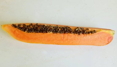 Üst ve düz taze, olgun bir papaya meyvesi uzanıyor. Tohumları, yemek dokusunu, kesimini, kesilmiş meyveleri beyaz bir zeminde izole edilmiş. Sağlıklı beslenme için sebze ve meyve